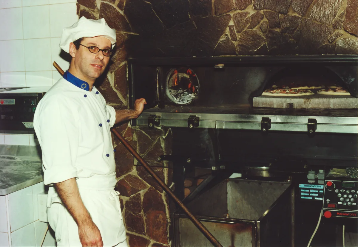 Giuseppe Irranca in giacca da pizzaiolo davanti al forno a legna con due pizze in cottura